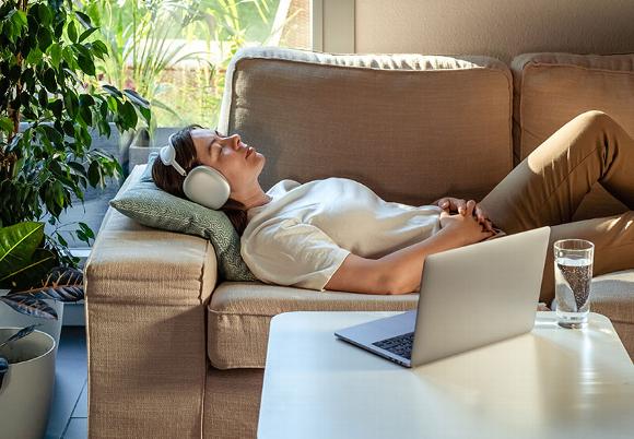 Person relaxing on a couch with headphones and a laptop nearby, enjoying remote Reiki healing.