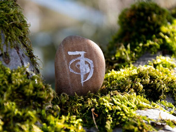 A smooth stone with a Reiki symbol resting on green moss.