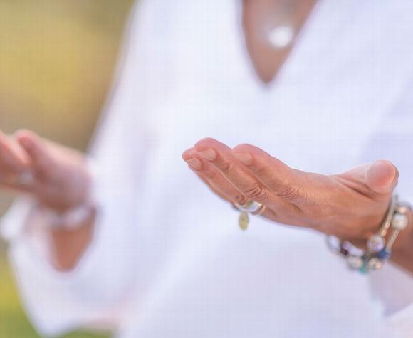 Hands held in a healing gesture, dressed in a white top, symbolizing Reiki energy work.
